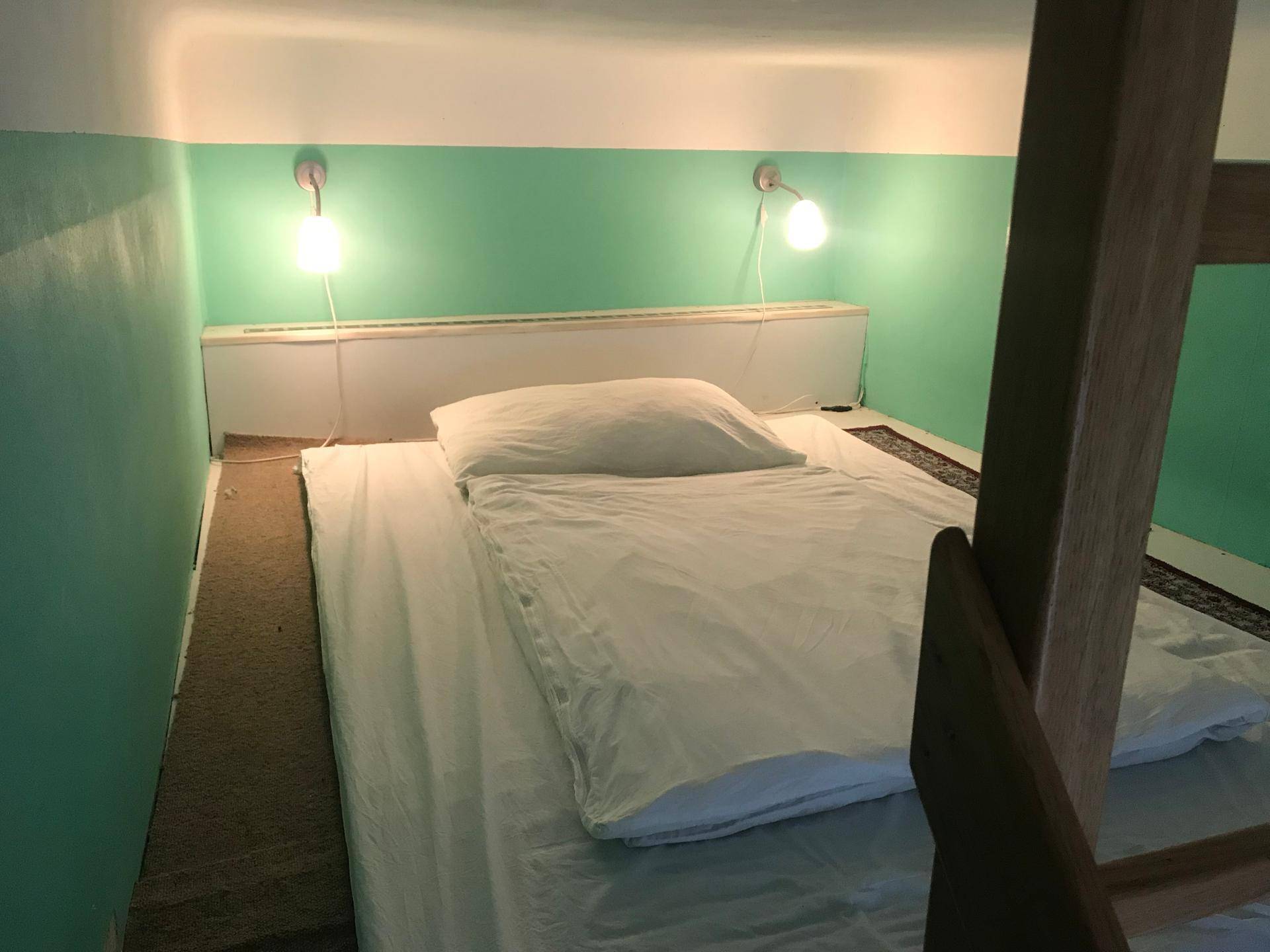 Gemütliches Hochbett mit weißer Bettwäsche, grünen Wänden und zwei Wandlampen für Leselicht.