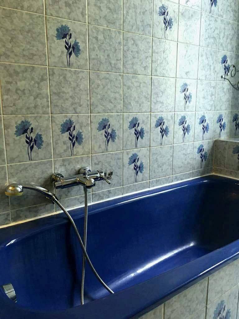 Badezimmer mit einer auffälligen blauen Badewanne und grauen Fliesen mit floralem Muster an den Wänden.