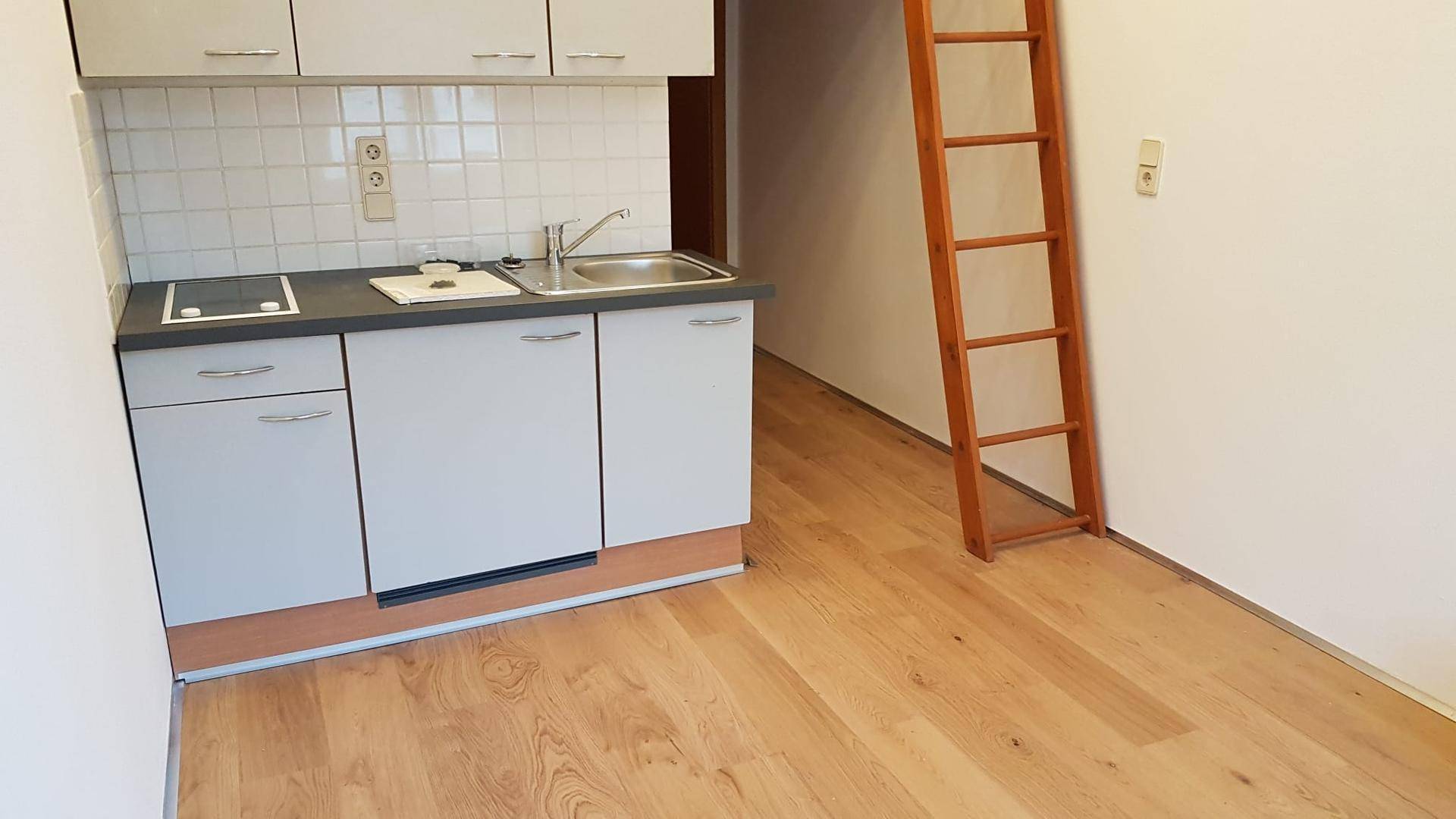 Kompakte Küchenzeile mit Spüle und Kochfeld, ergänzt durch eine Holzleiter, die zu einem oberen Bereich führt.