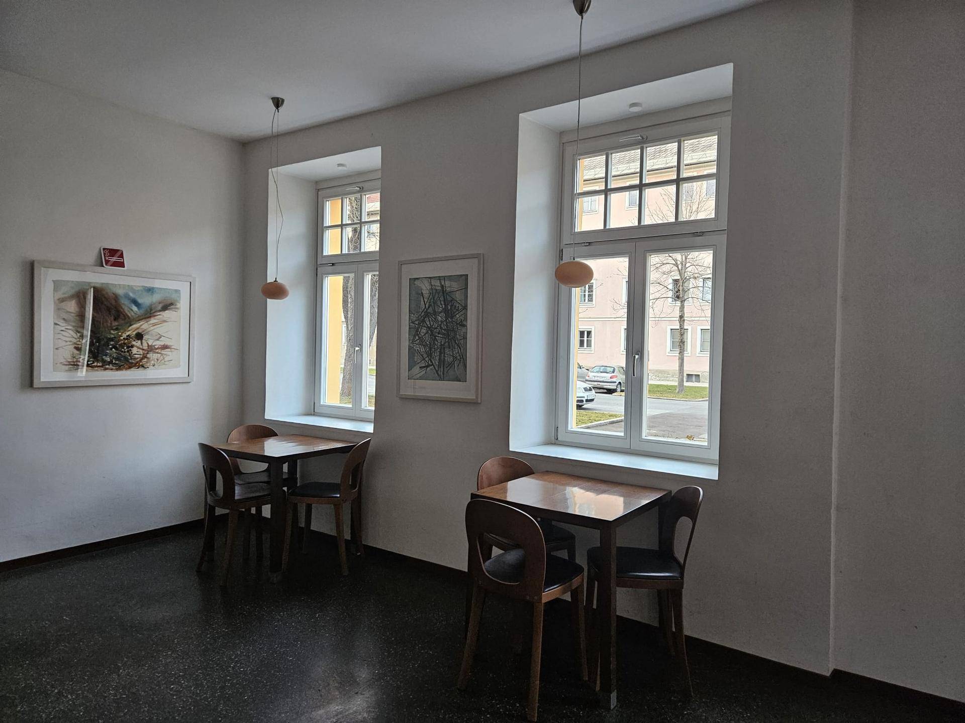Heller Gewerberaum mit zwei Tischen, Stühlen und großen Fenstern, die auf die Straße blicken.