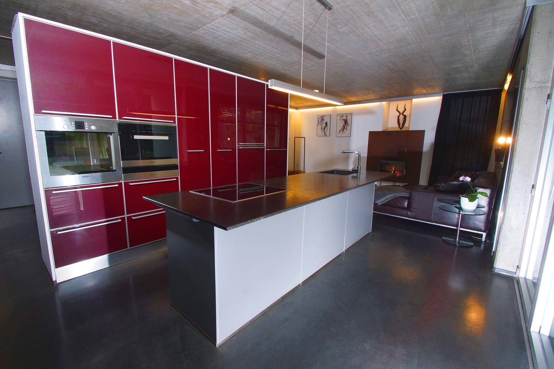 Offene Wohnküche mit roten Schränken, Kücheninsel und gemütlichem Wohnbereich mit Kamin.