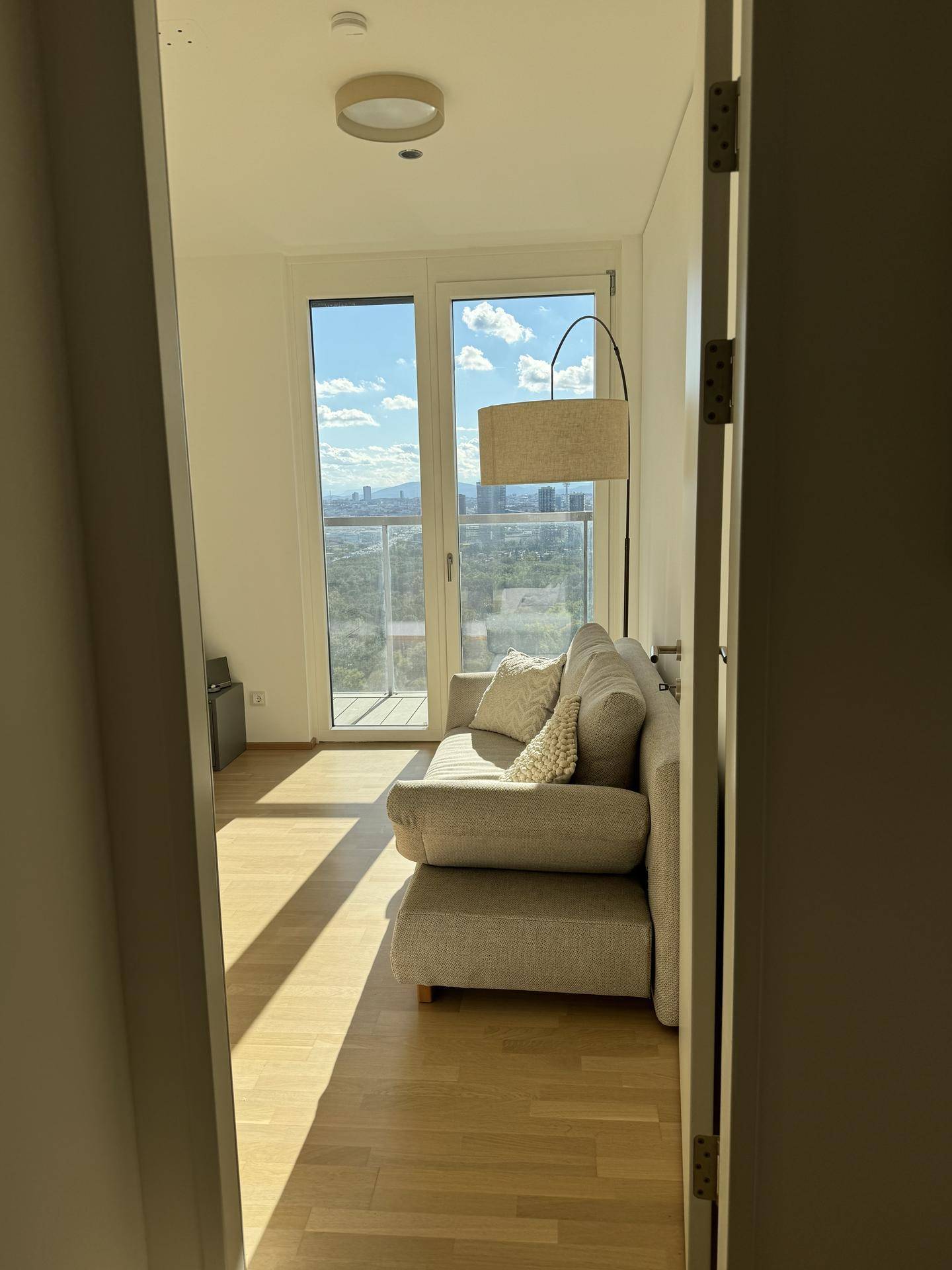 Helles Zimmer mit Sofa, Holzboden und Zugang zu einem Balkon mit Stadtblick.