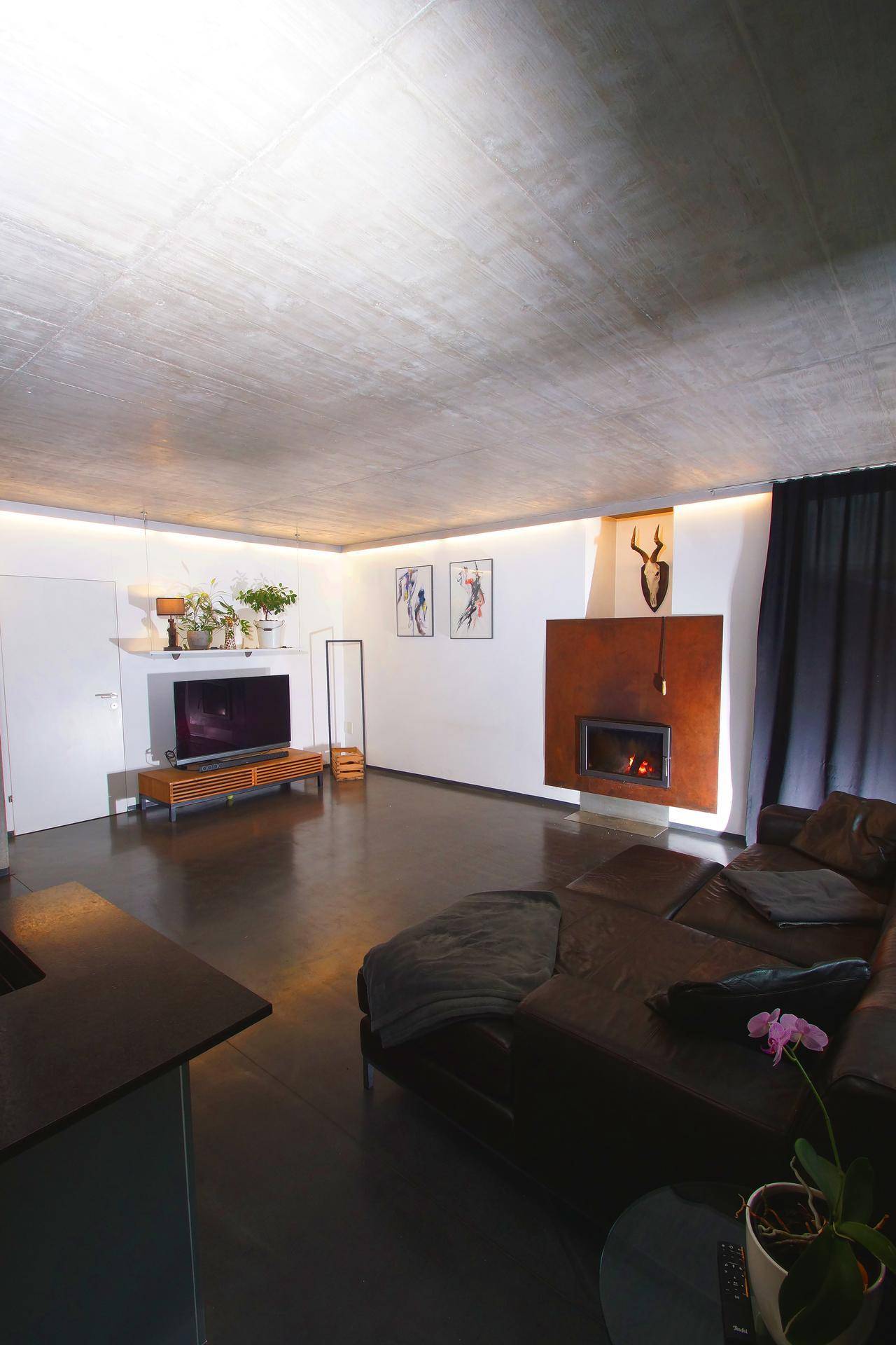 Geräumiges Wohnzimmer mit modernem Kamin, großer Couch und indirekter Beleuchtung.