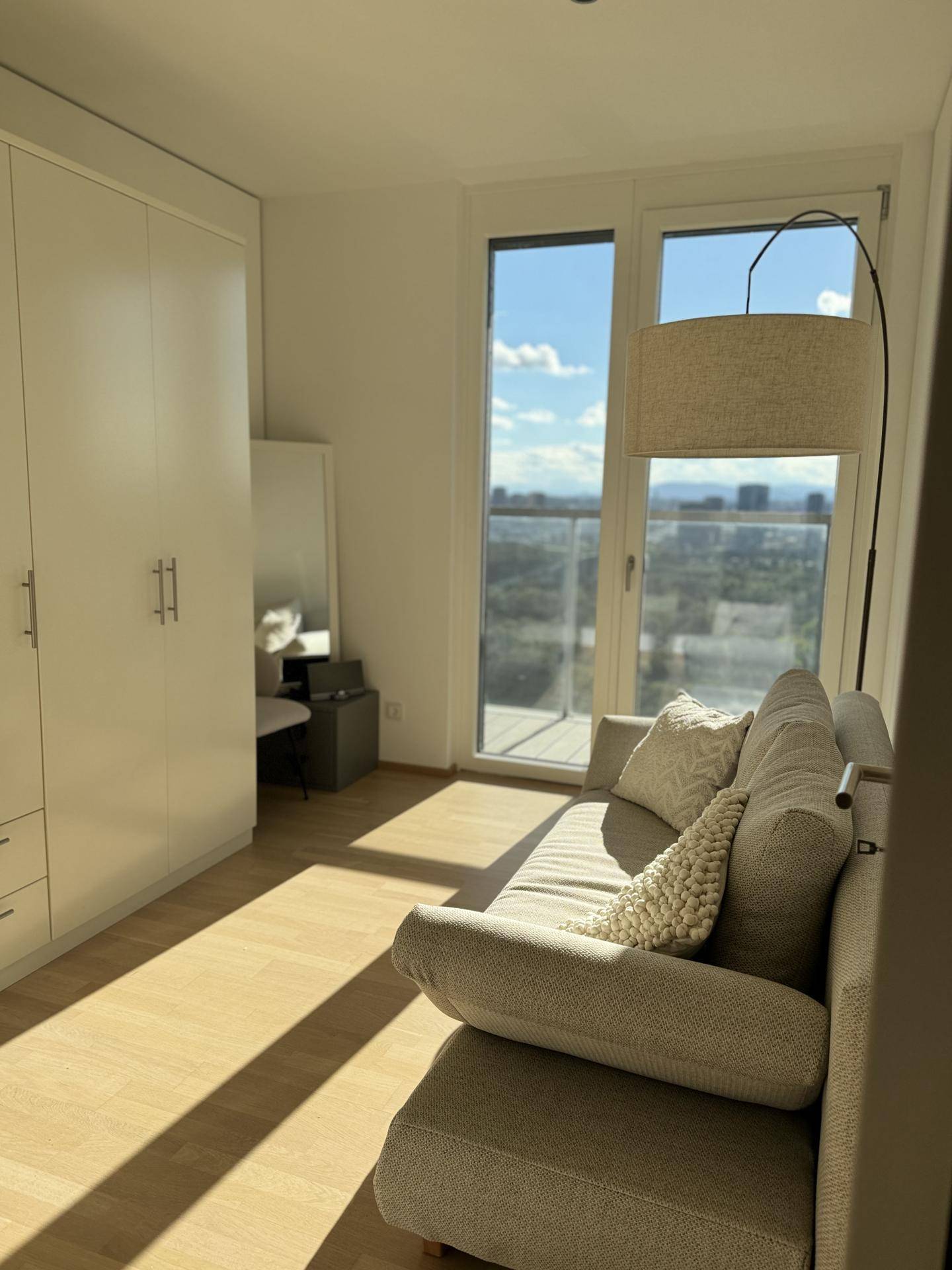 Helles Zimmer mit Sofa, integrierten Einbauschränken und Zugang zum Balkon.
