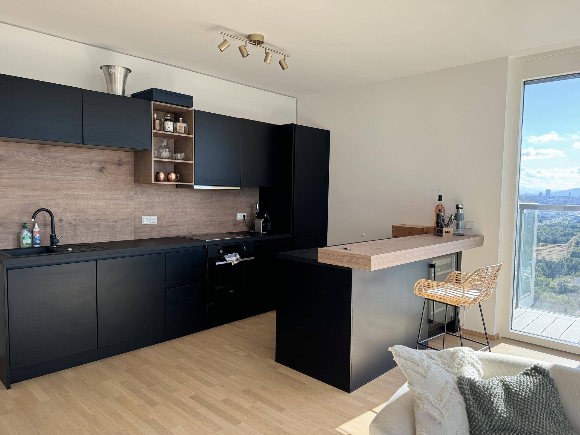 Moderne Küche mit schwarzen Schränken, Holzakzenten, Frühstücksbar und Stadtblick.