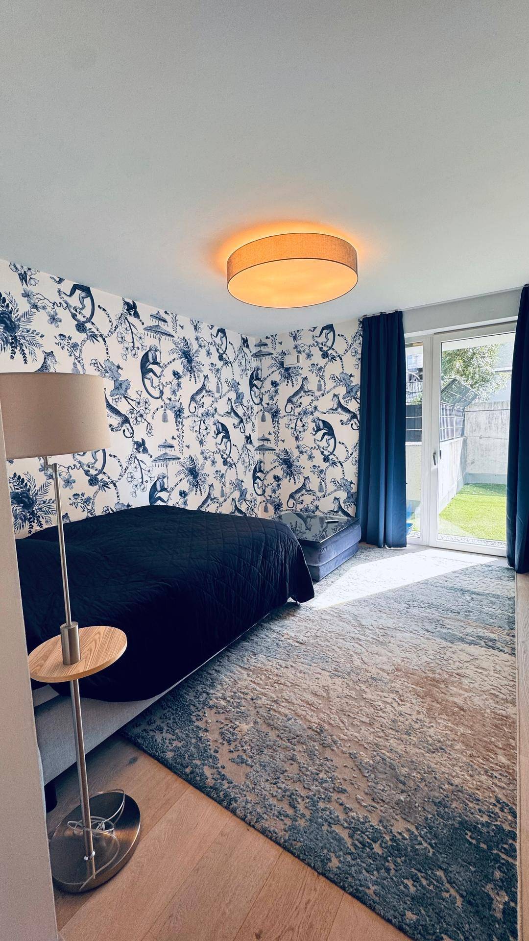 Gemütliches Schlafzimmer mit auffälliger blauer Tapete, Holzboden und direktem Zugang zum Garten.