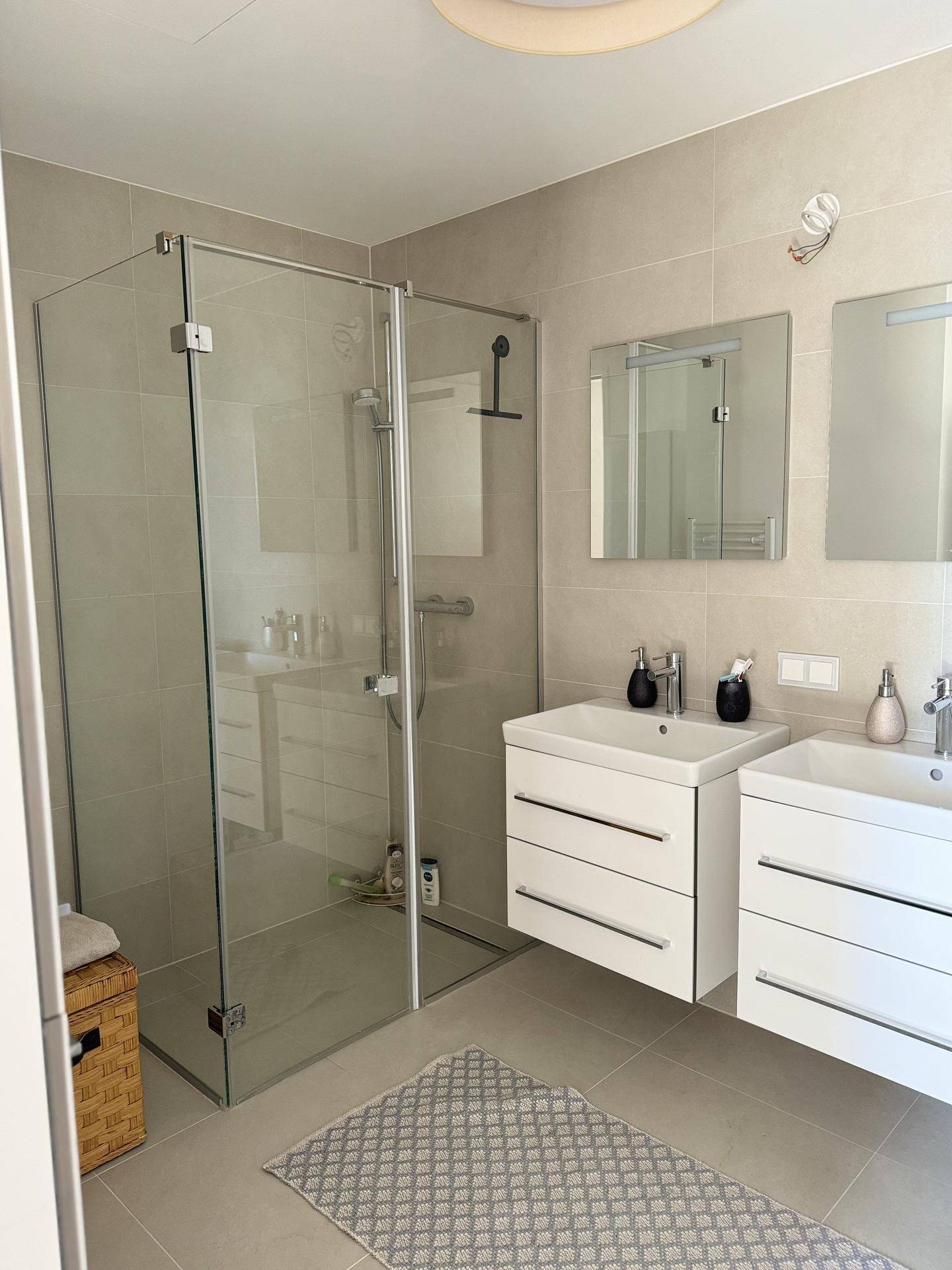 Modernes Badezimmer mit Doppelwaschbecken, ebenerdiger Dusche und hellen Fliesen.
