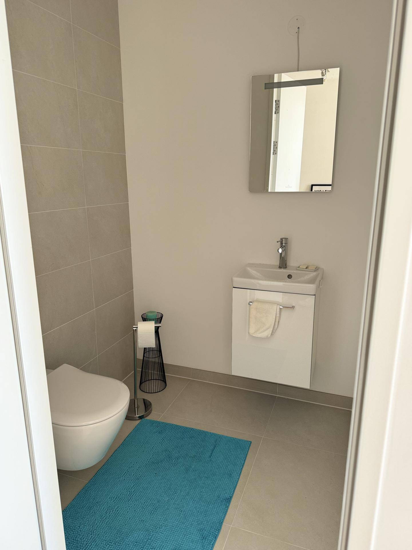 Kleines Gäste-WC mit modernem Waschbecken, Wand-WC und hellen Fliesen.
