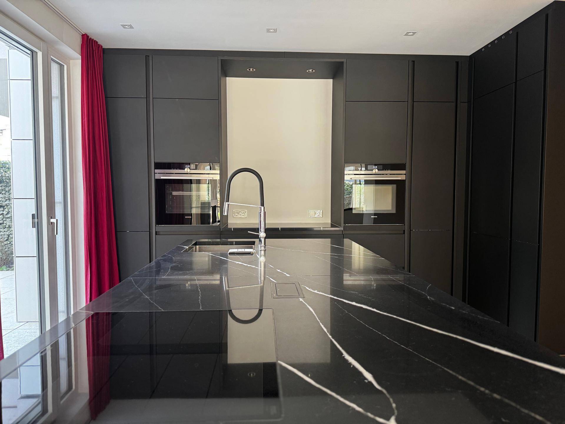 Elegante schwarze Kücheninsel mit Marmorarbeitsplatte und integriertem Spülbecken, umgeben von modernen Einbaugeräten.