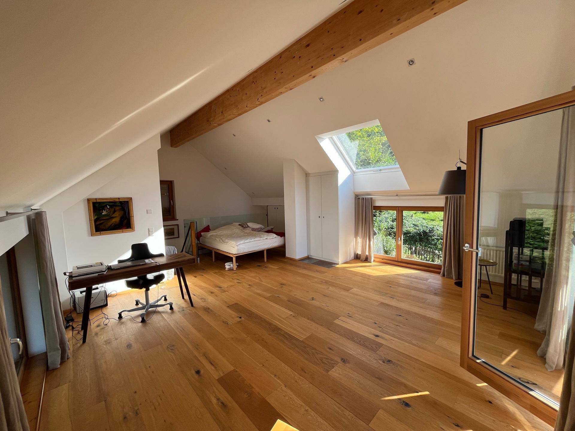 Geräumiges Schlafzimmer im Dachgeschoss mit Holzboden, Schreibtisch und Dachfenster.