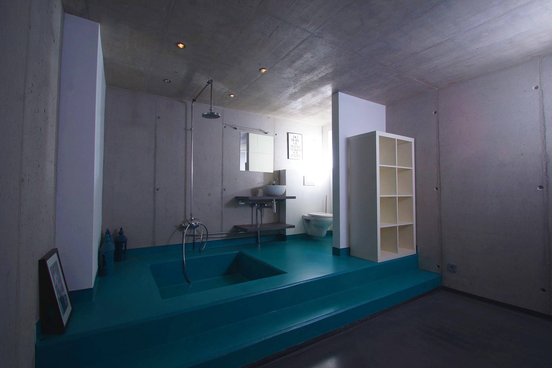 Einzigartiges Badezimmer mit erhöhter blauer Duschwanne, Betonwänden und minimalistischem Design.
