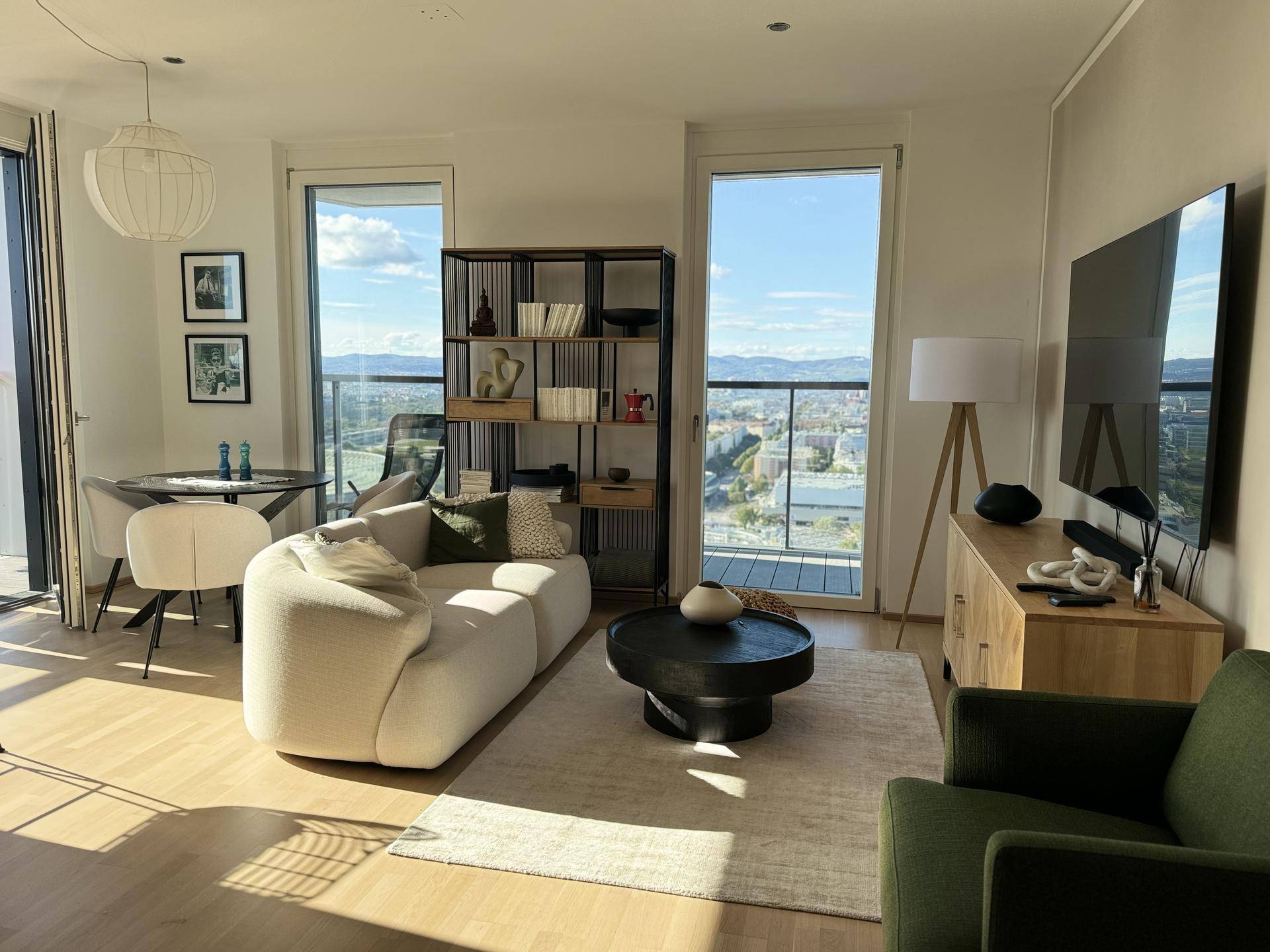 Lichtdurchflutetes Wohnzimmer mit Fernseher, Sofa und Panoramablick auf die Stadt.
