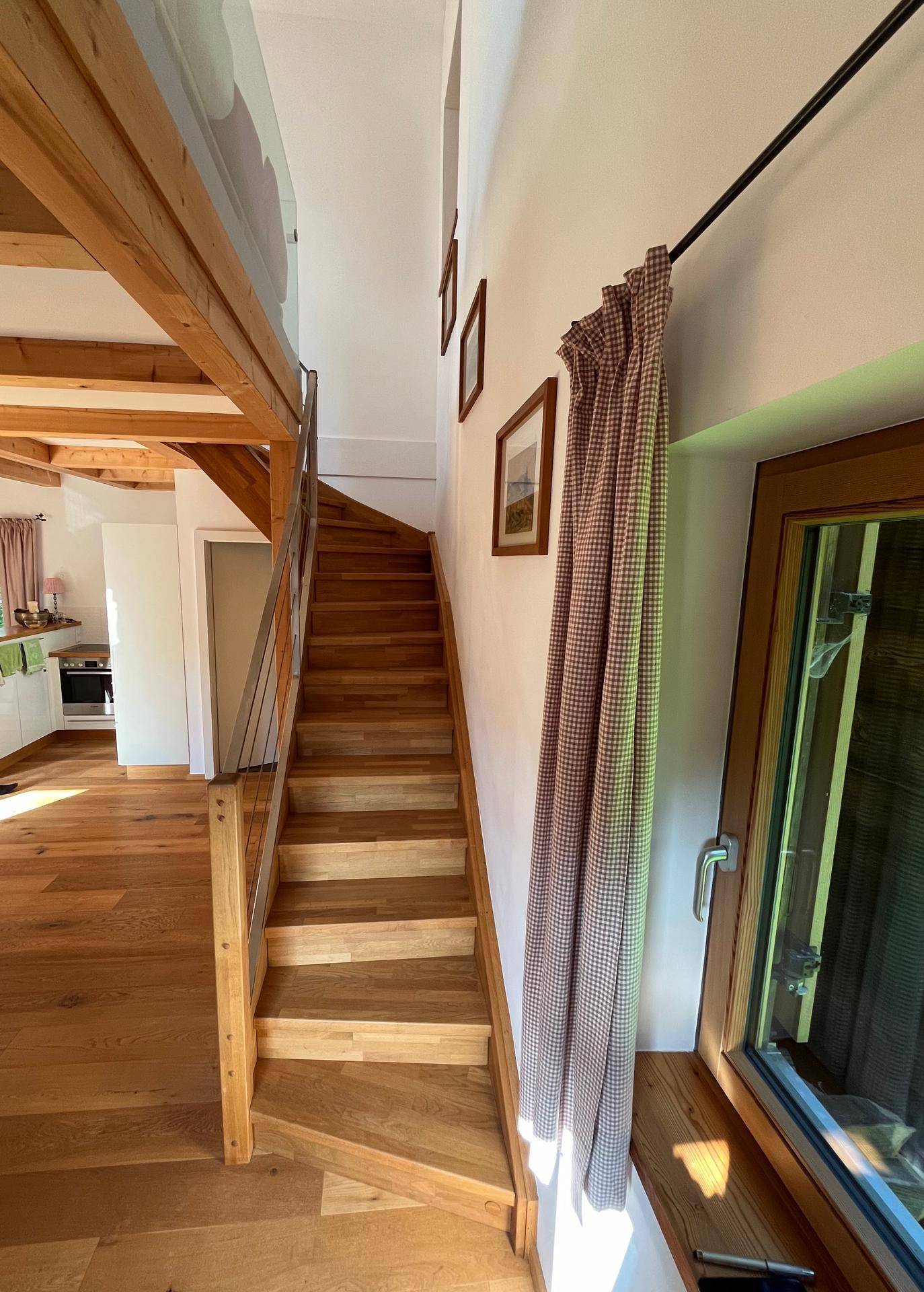 Holztreppe führt in die obere Etage, mit natürlichem Lichteinfall durch ein Fenster.