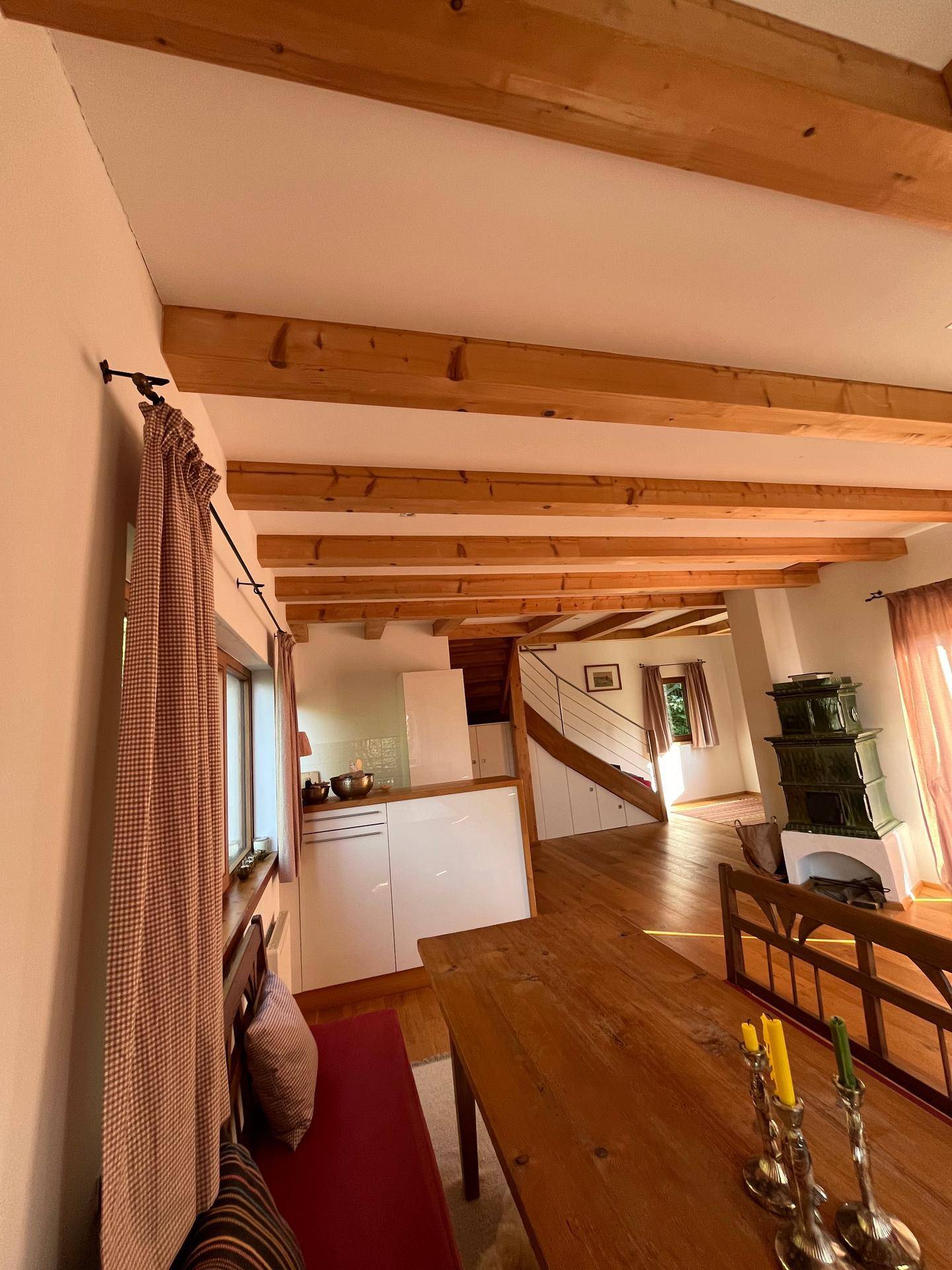 Essbereich mit Holztisch und Blick auf die offene Küche und den Kachelofen.