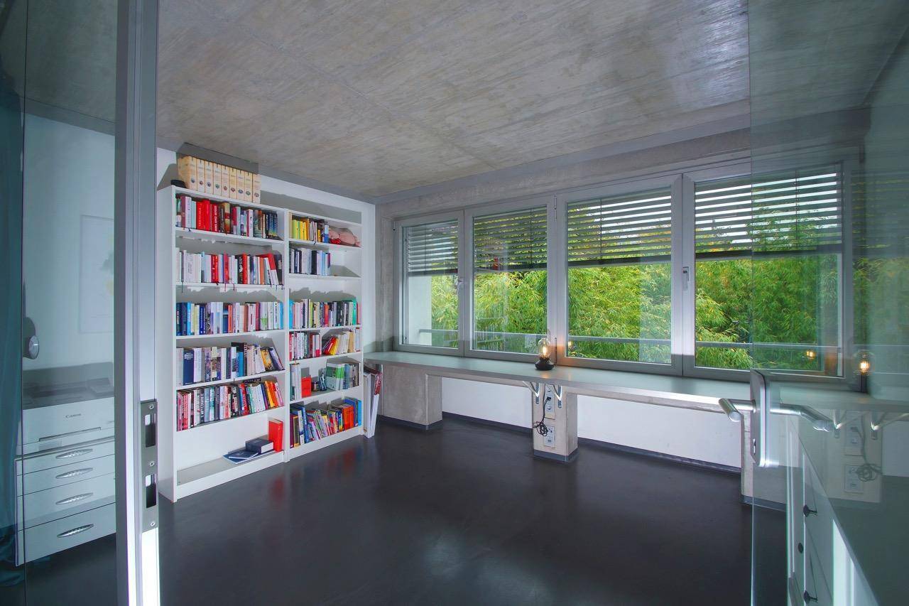 Helles Arbeitszimmer mit großem Bücherregal, Schreibtisch und weitem Blick ins Grüne.