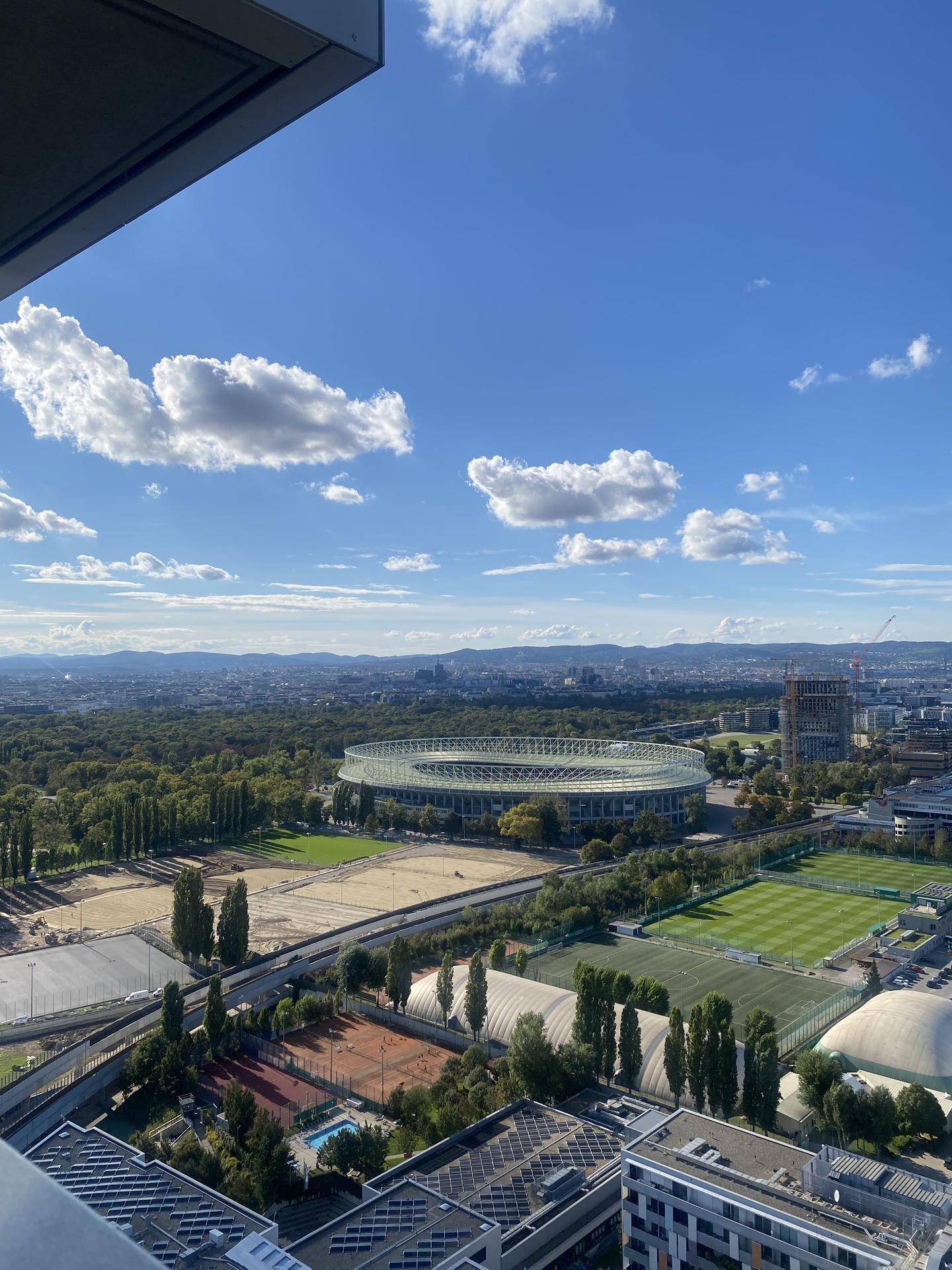 Weite Aussicht auf die Stadt, das Stadion und grüne Parkanlagen unter blauem Himmel.