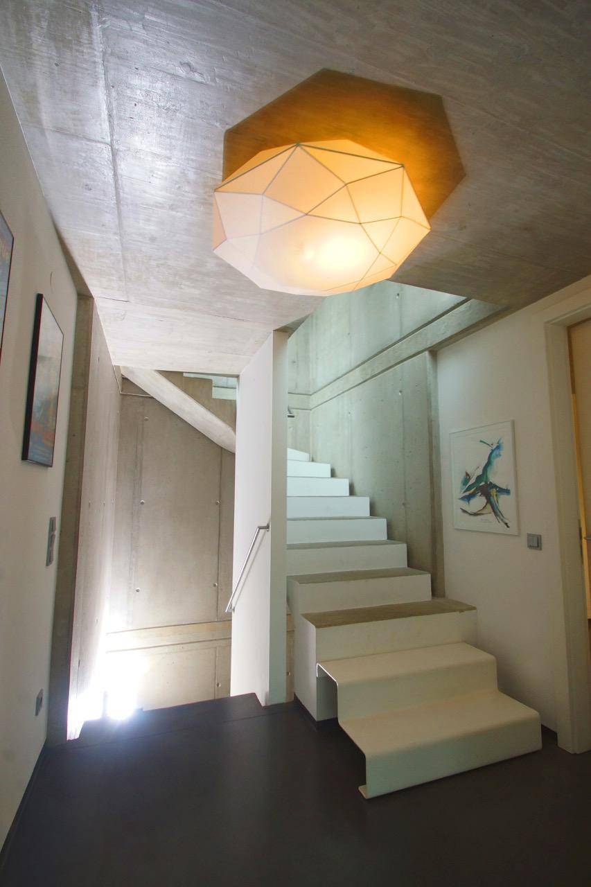 Heller Flur mit moderner weißer Treppe und Sichtbetonwänden, gut beleuchtet.