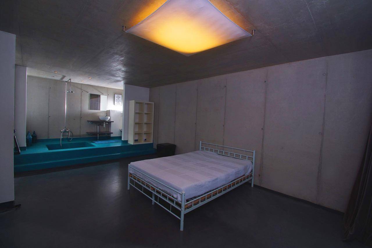 Schlafzimmer mit minimalistischem Bett und offenem Zugang zu einem modernen Badebereich.