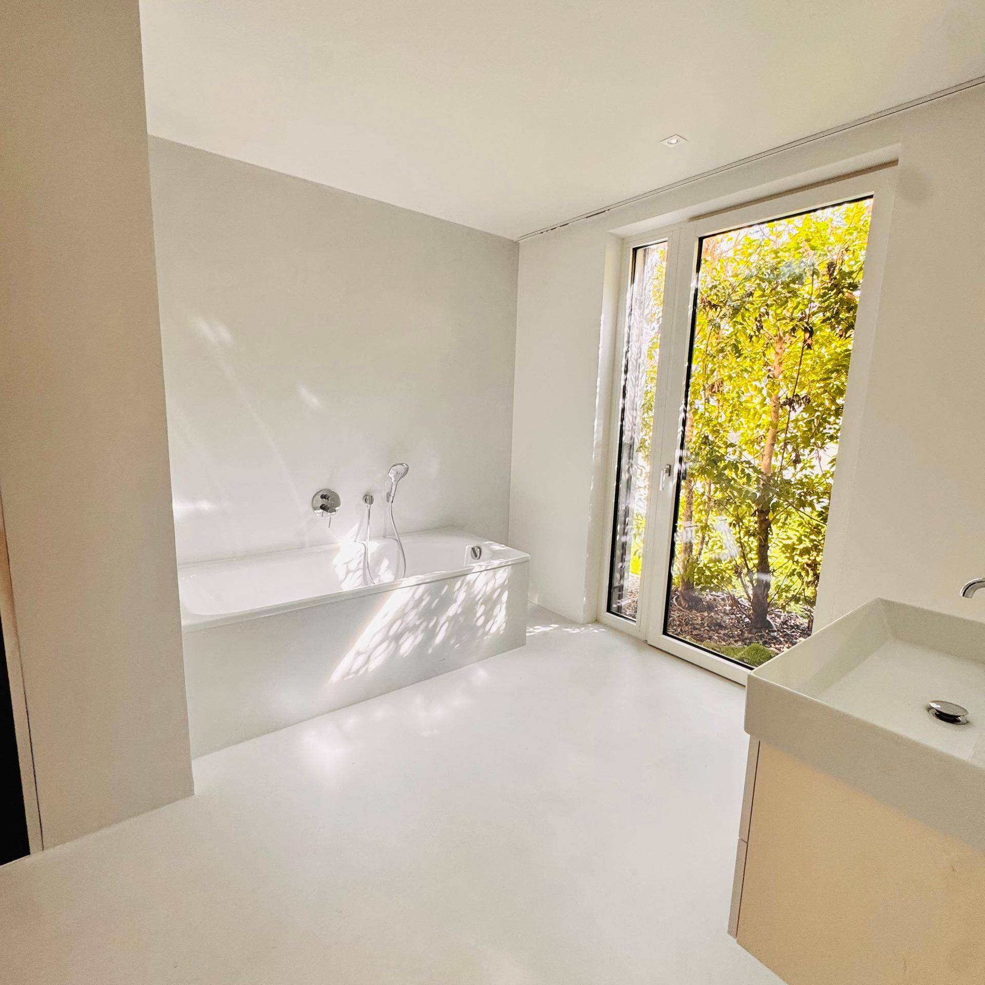 Helles Badezimmer mit Badewanne, modernem Waschbecken und großem Fenster mit Blick ins Grüne.
