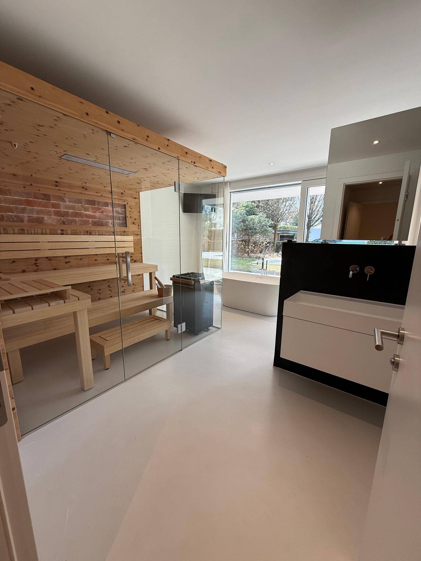 Geräumiges Badezimmer mit integrierter Sauna, modernem Waschbecken und großem Fenster mit Blick ins Freie.