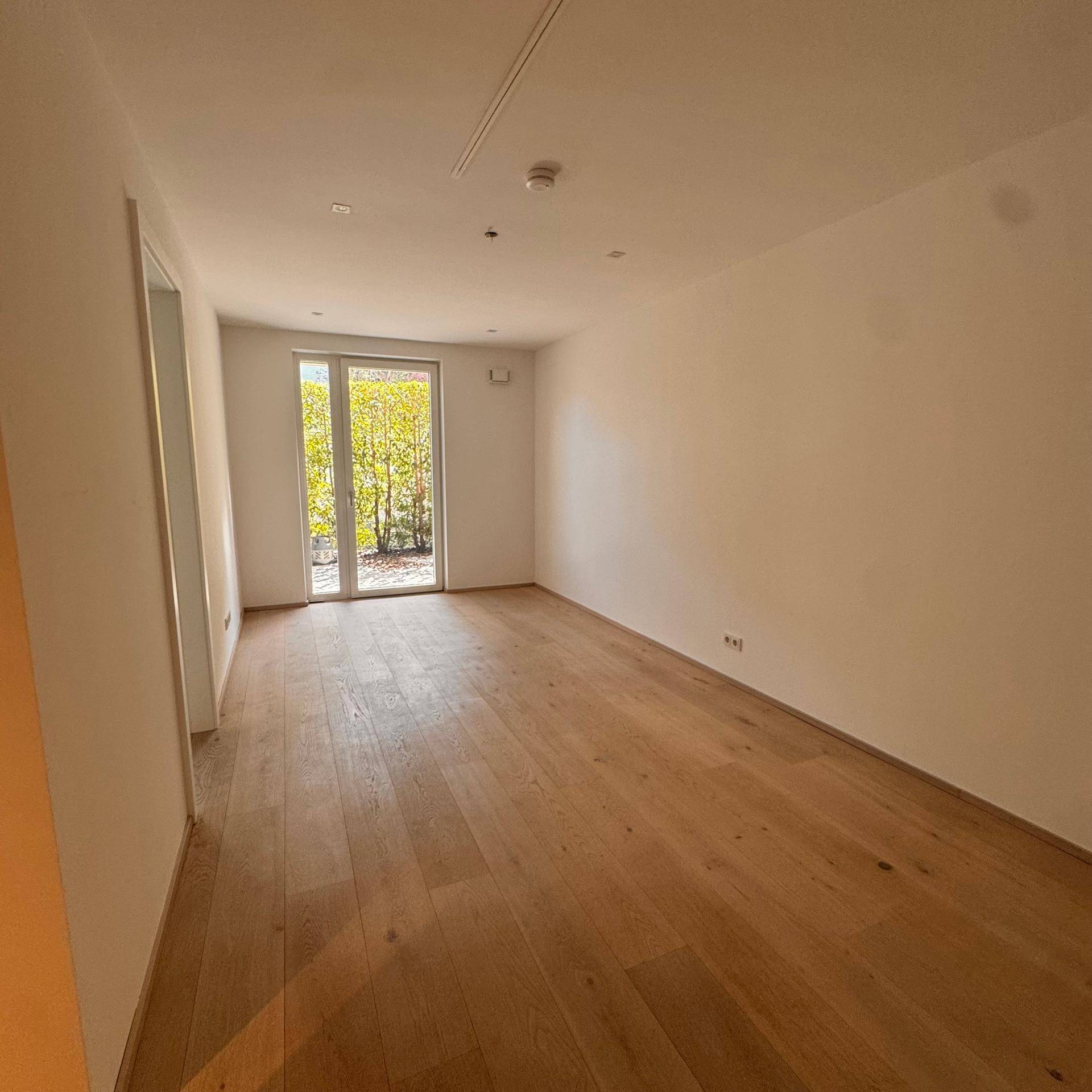 Geräumiges Schlafzimmer mit hellem Holzboden und Fensterfront, die einen Blick ins Grüne bietet.