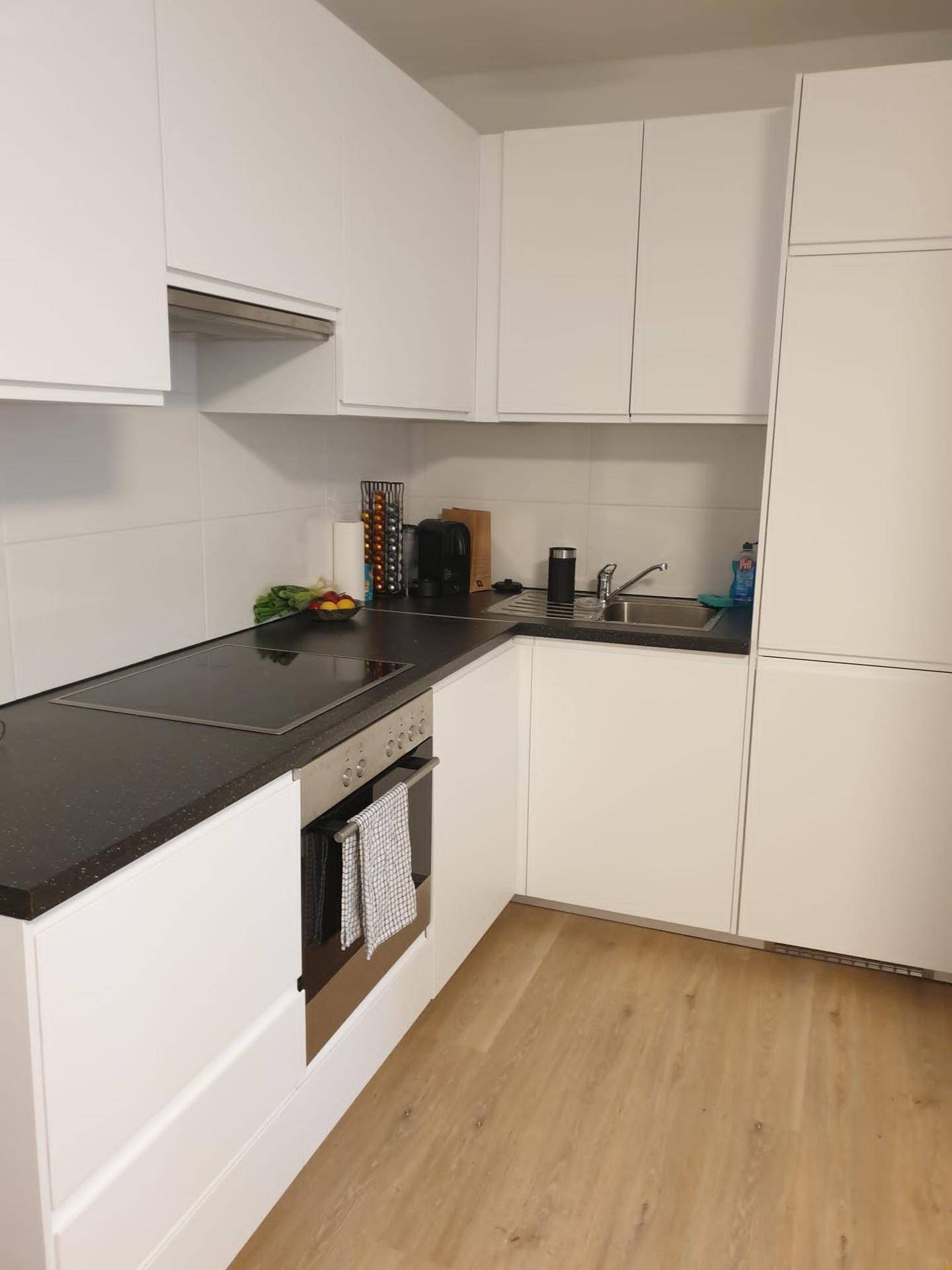 Moderne Einbauküche mit weißen Schränken, dunkler Arbeitsplatte und Kochfeld.