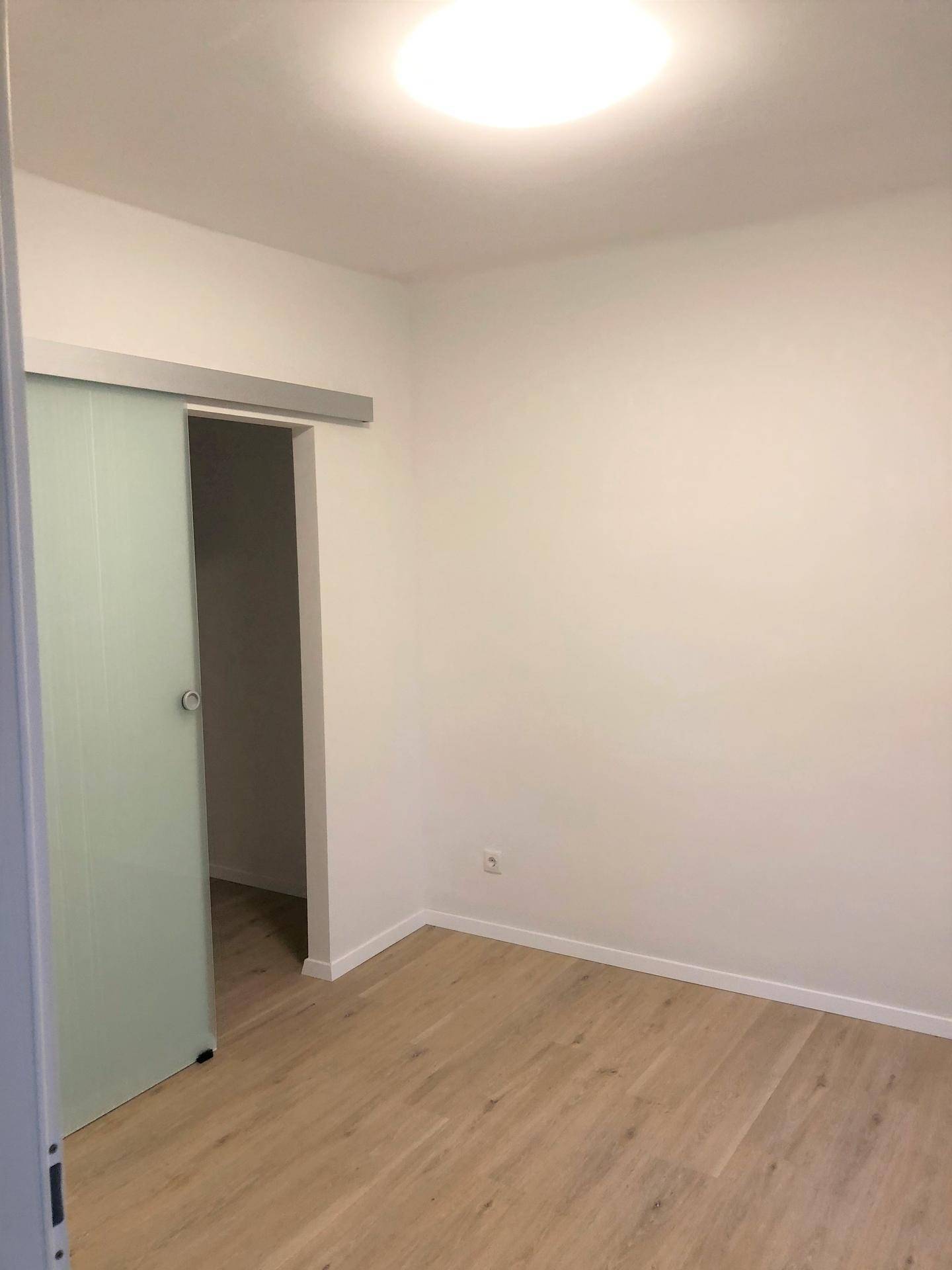 Helles Zimmer mit Schiebetür und Laminatboden, ideal als Schlaf- oder Arbeitszimmer.