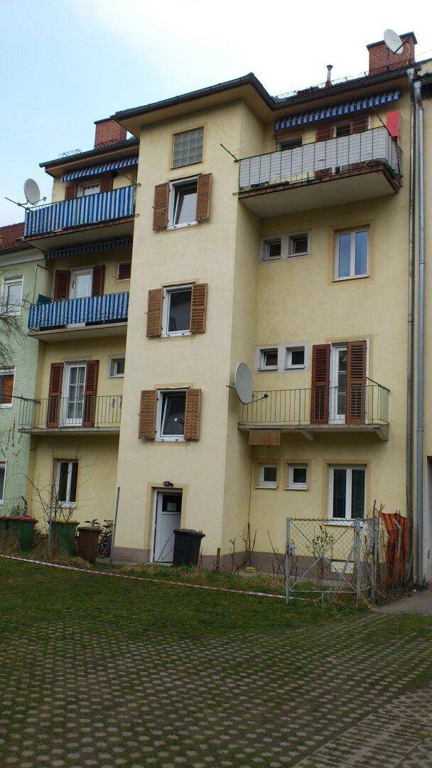 Gelbe Fassade eines Mehrfamilienhauses mit mehreren Balkonen, blauen Geländern und braunen Fensterläden.