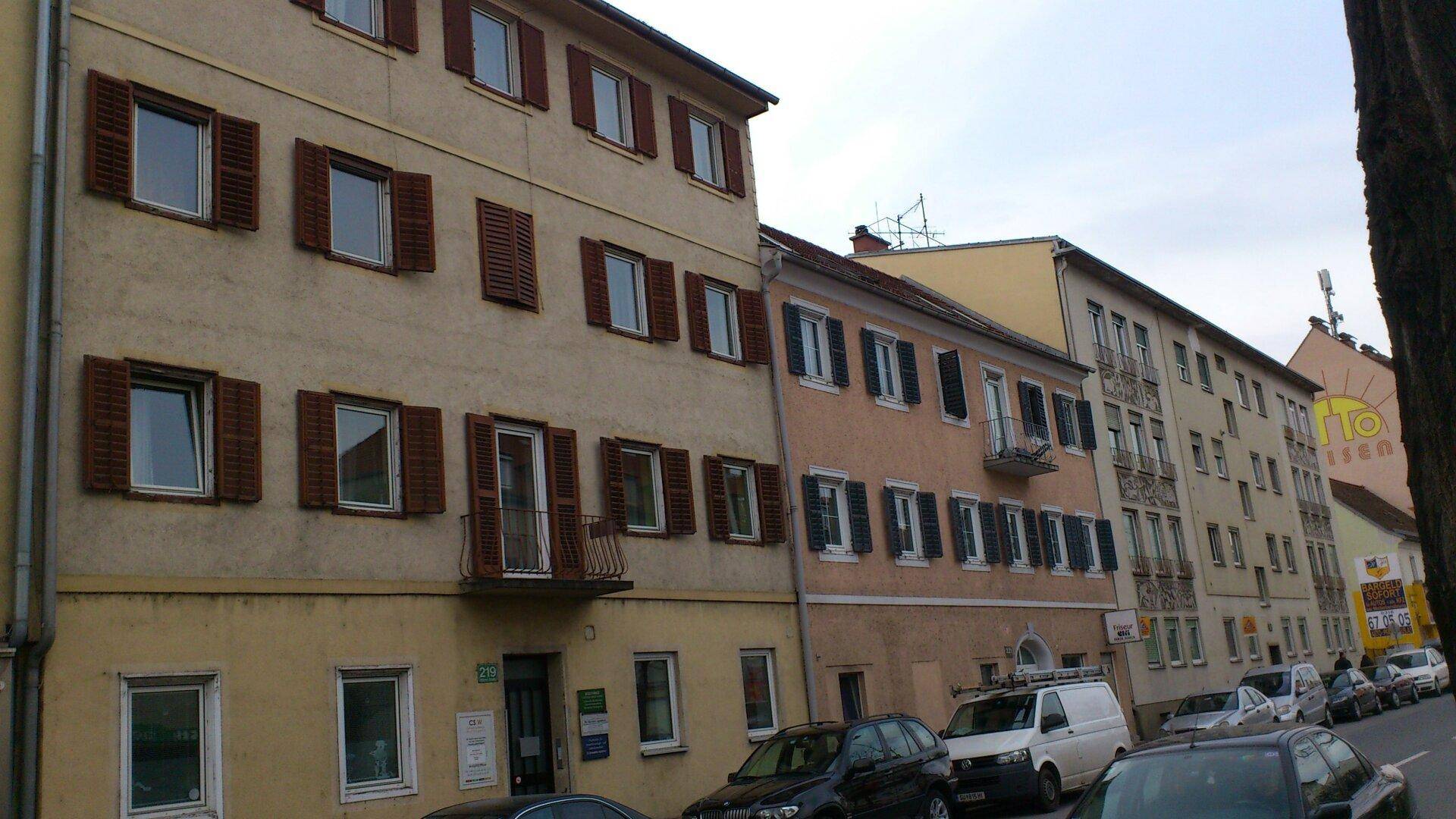 Straßenansicht einer Reihe von älteren Wohngebäuden mit traditionellen Fensterläden und parkenden Autos.
