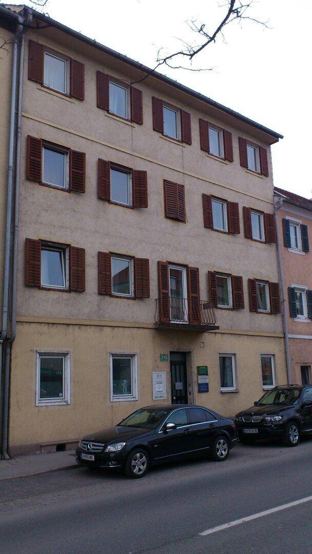 Fassade eines älteren Mehrfamilienhauses mit braunen Fensterläden und einem kleinen französischen Balkon.