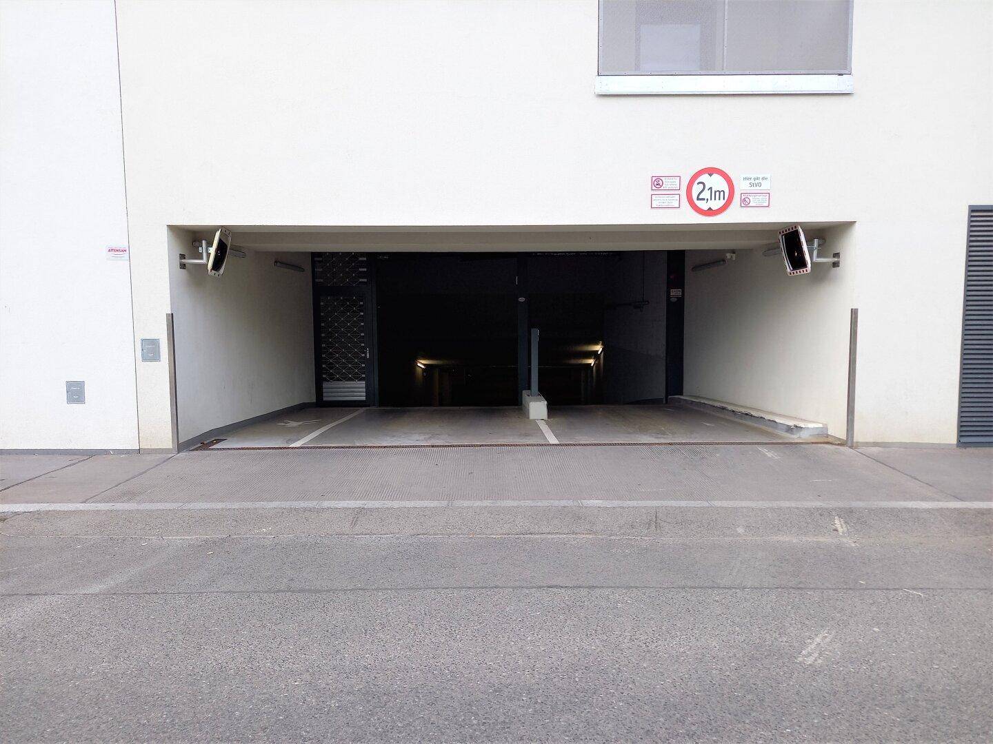 Eingang zur Tiefgarage mit Höhenbegrenzung und sichtbaren Überwachungskameras an der Fassade.