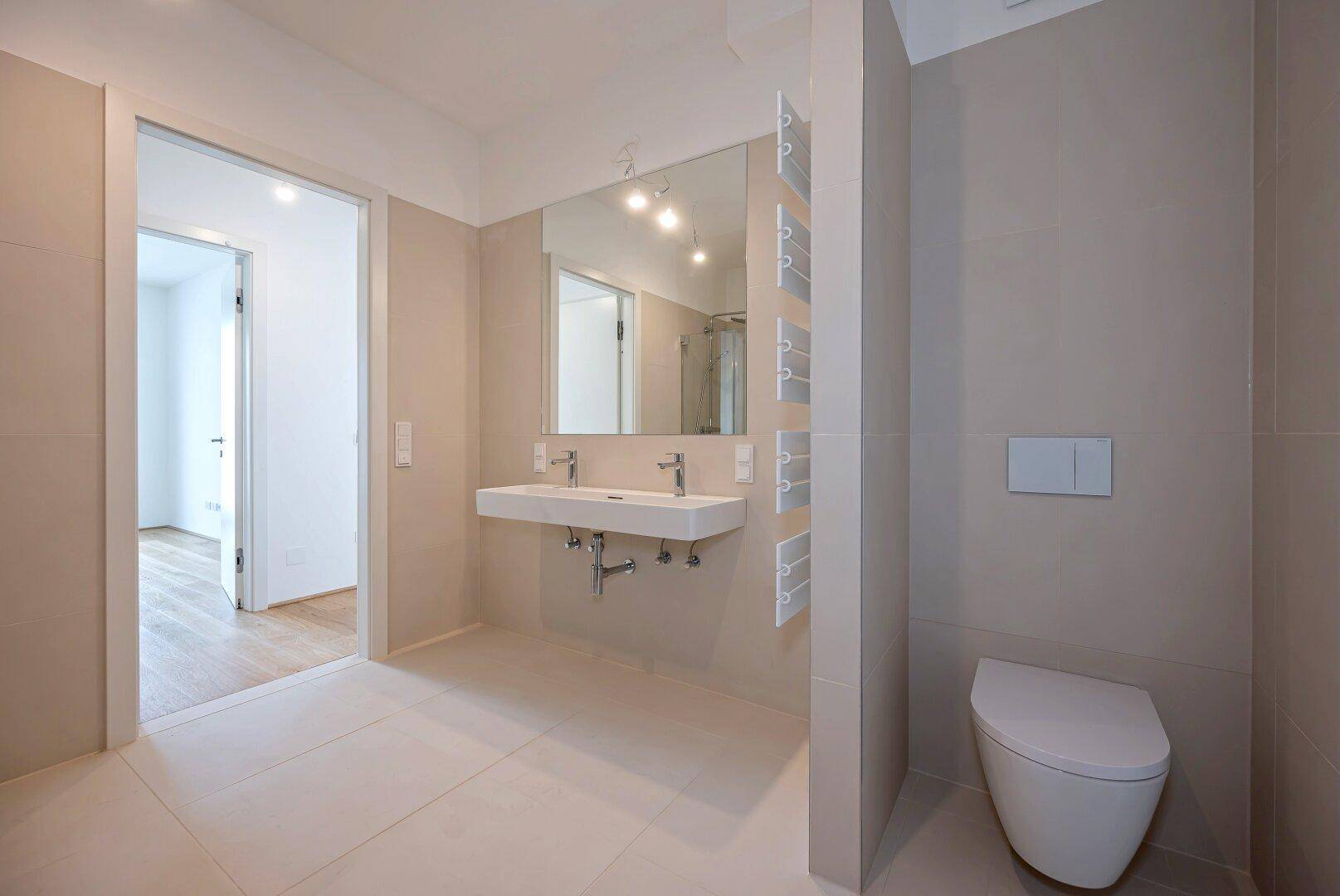 Geräumiges Badezimmer mit Doppelwaschbecken, Wand-WC und großem Spiegel.