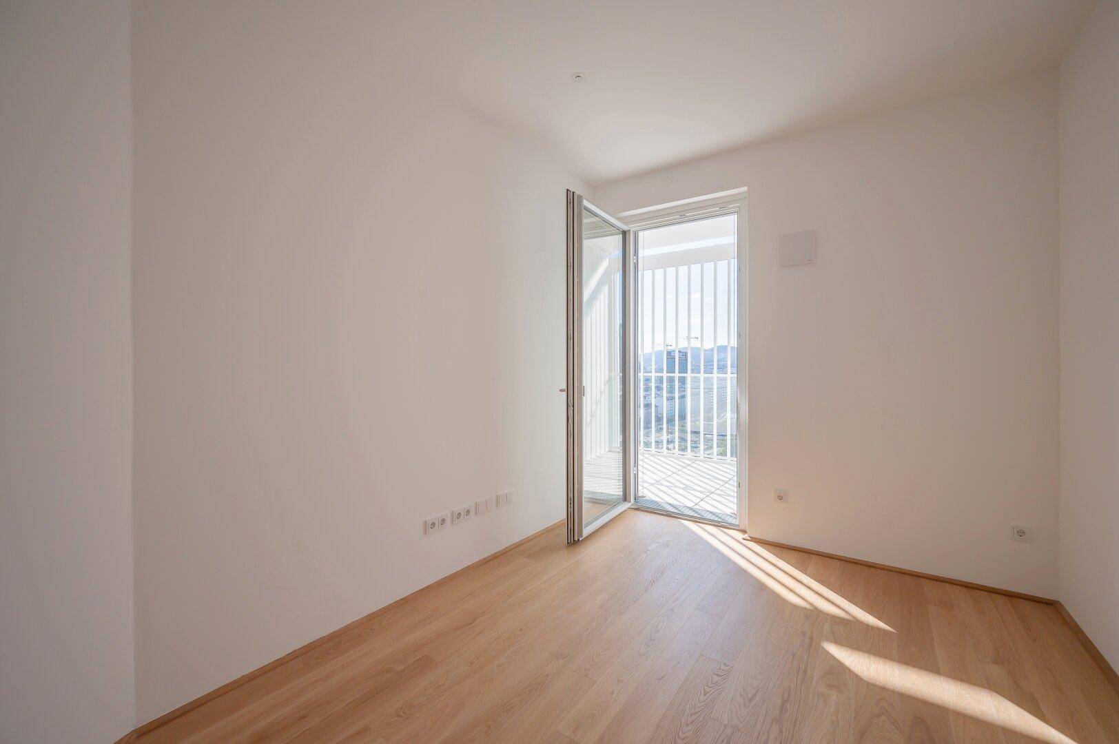 Sonniger Raum mit Holzboden und Balkontür, perfekt als Schlaf- oder Arbeitszimmer nutzbar.