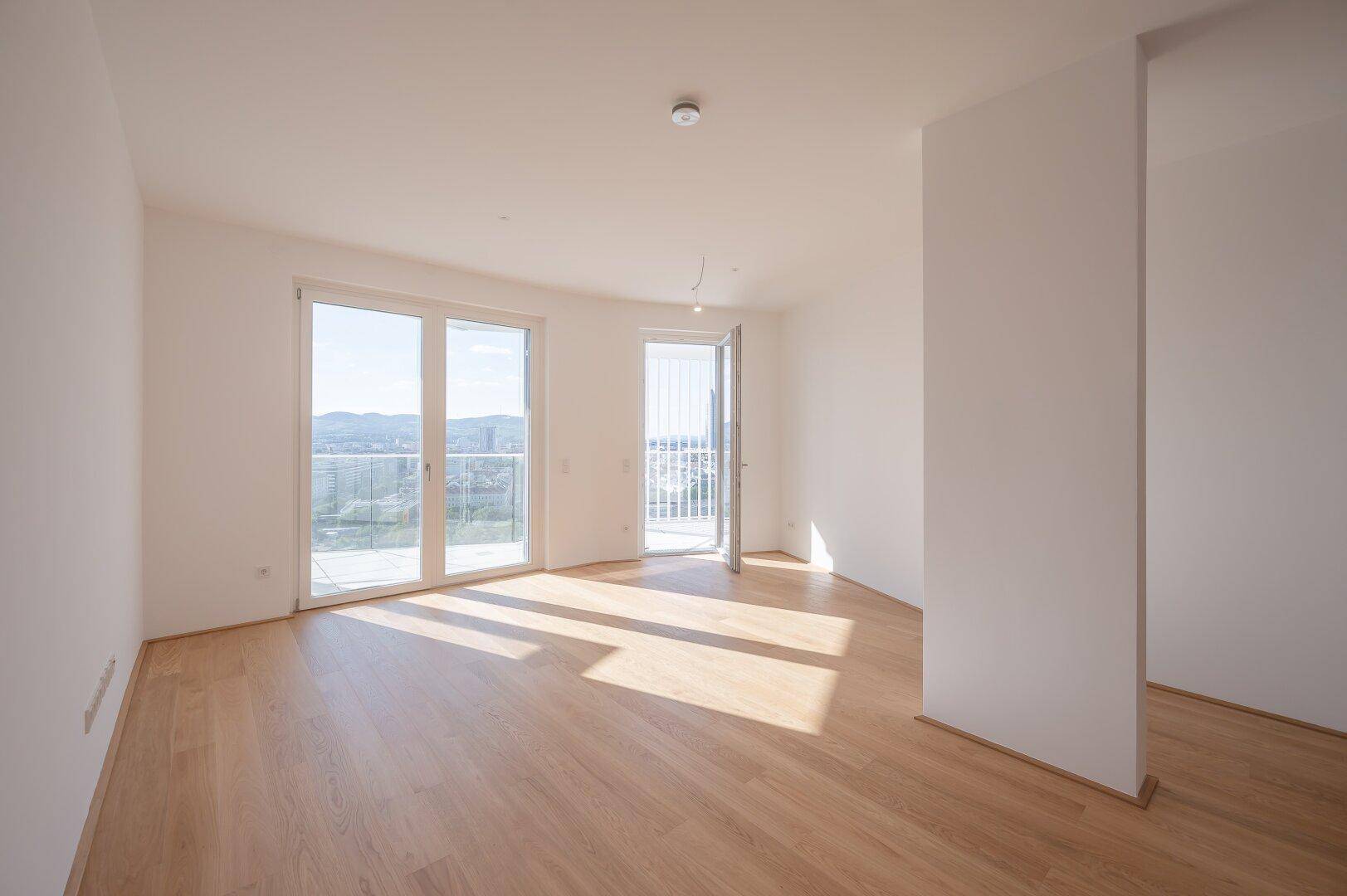 Geräumiges, helles Zimmer mit Holzboden und Zugang zu einem Balkon, ideal als Wohnbereich.