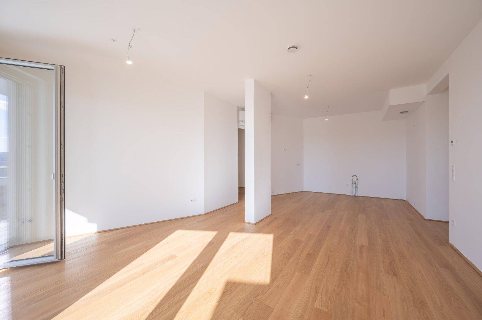 Heller, leerer Raum mit Holzboden und Balkonzugang, ideal für einen offenen Wohnbereich.