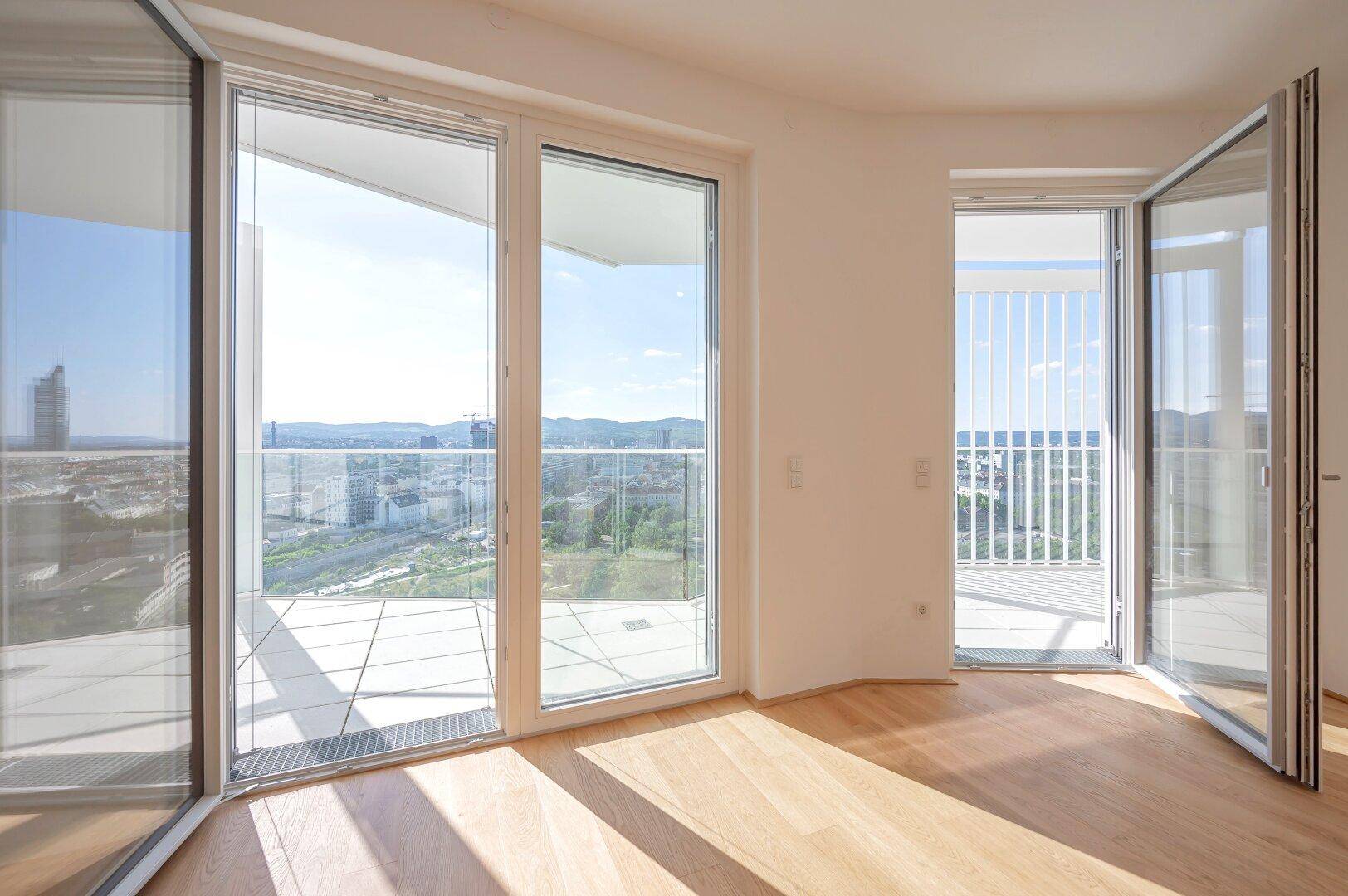 Helles Wohnzimmer mit Holzboden und großen Fenstern, die Zugang zu einem sonnigen Balkon bieten.