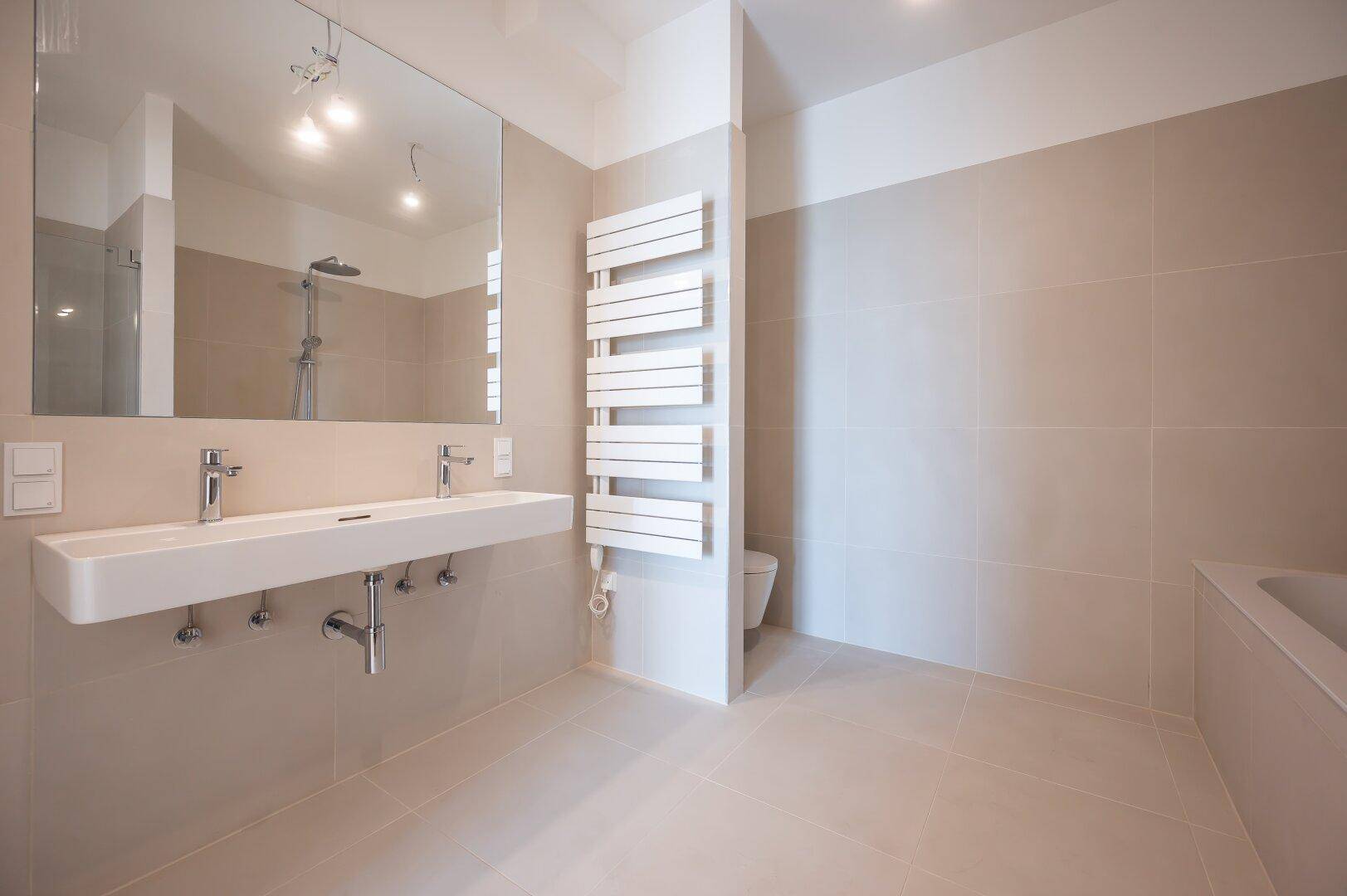 Modernes Badezimmer mit Doppelwaschbecken, beheiztem Handtuchhalter und WC.