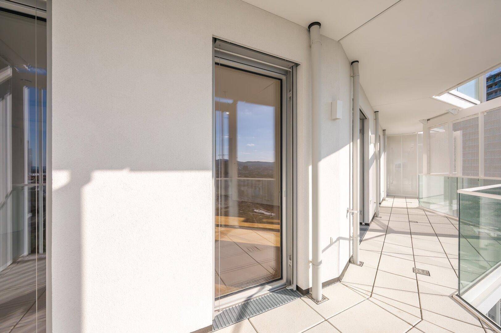 Langer, heller Balkon mit Fliesenboden und Zugang zu mehreren Räumen.