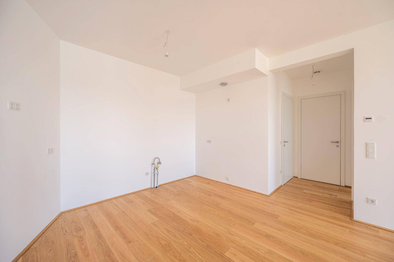 Heller Küchenbereich mit Holzboden und Anschlüssen, bereit für die Installation einer Einbauküche.