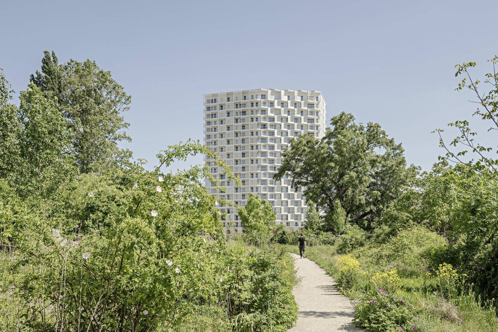 Modernes Wohngebäude umgeben von üppiger grüner Landschaft und einem Spazierweg.