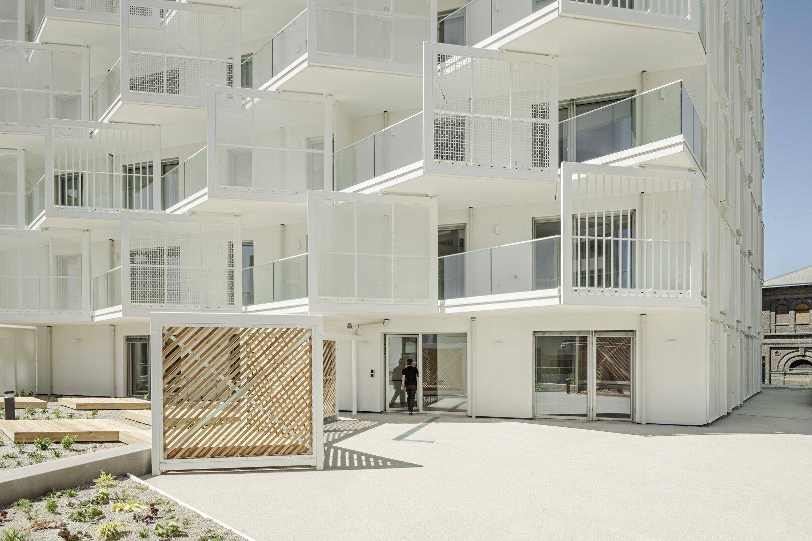 Eingangsbereich eines modernen Wohngebäudes mit kreativer Holzverkleidung und Balkonen.