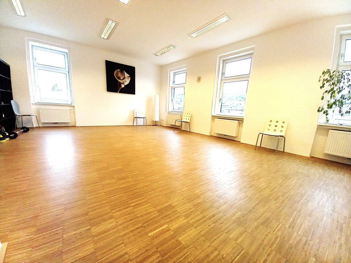 Geräumiger, heller Büroraum mit Holzparkett, großen Fenstern und moderner Beleuchtung, ausgestattet mit einigen Möbeln.