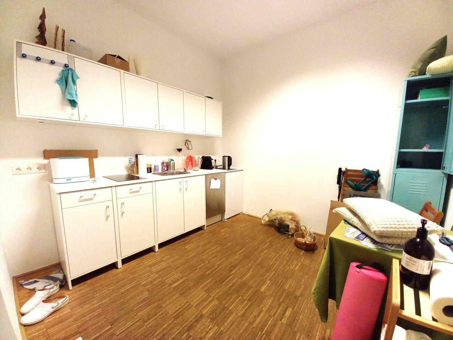 Kleine Küche mit weißen Hängeschränken, Spüle und Geschirrspüler, ergänzt durch einen Holzfußboden.