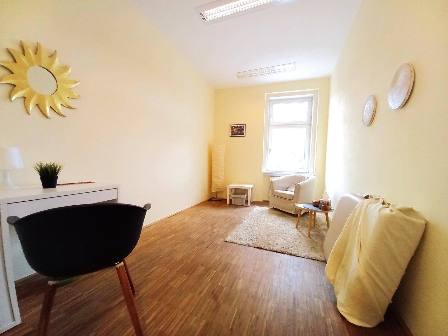 Gemütlicher Beratungsraum mit gelben Wänden, Holzfußboden und einem Fenster, eingerichtet mit Sessel und Schreibtisch.