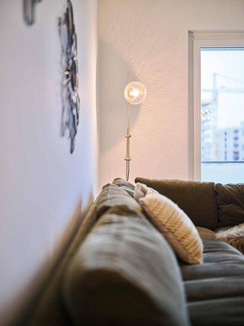 Detailansicht des Sofas und einer Stehlampe neben einem großen Fenster.