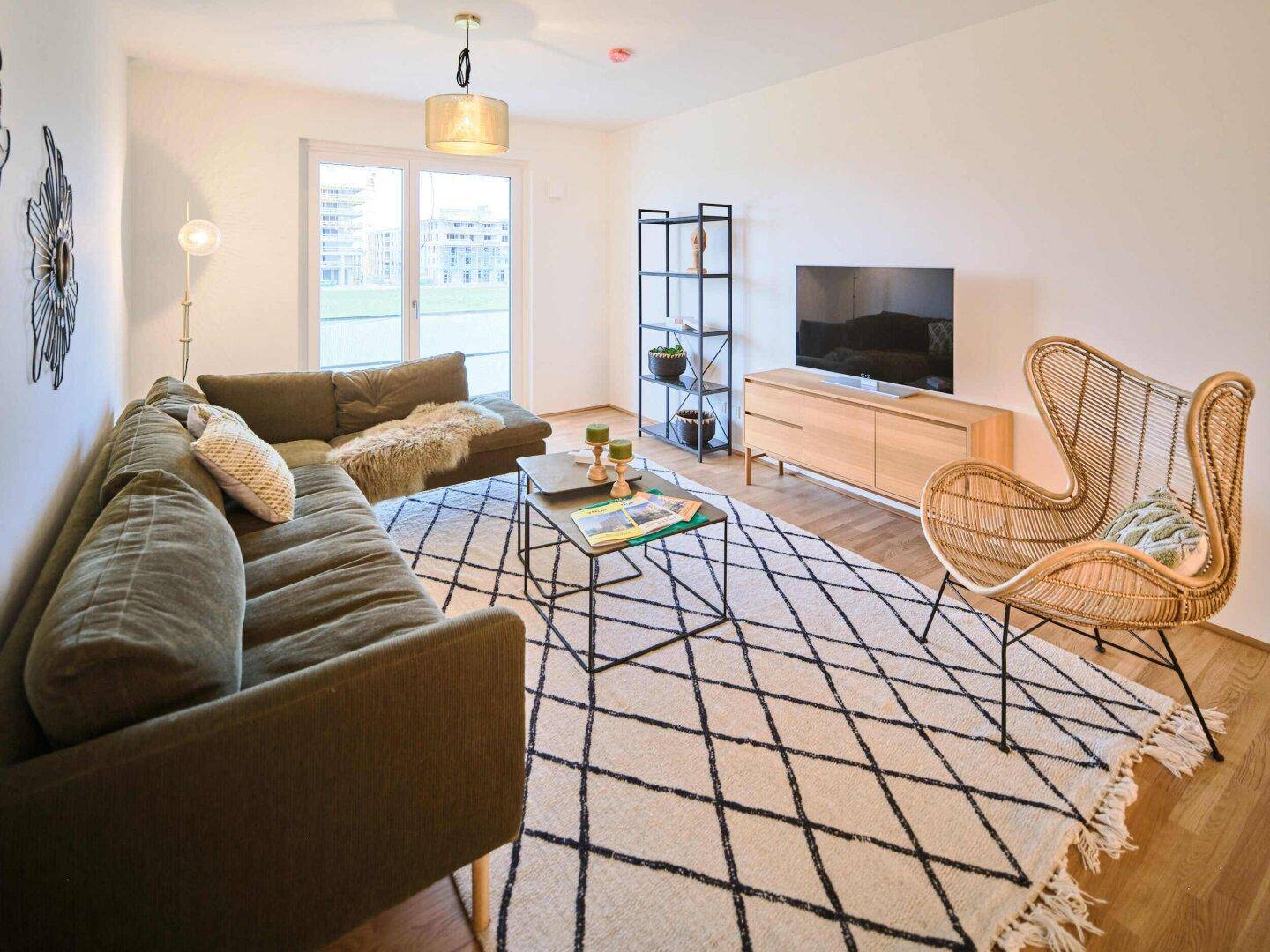 Helles Wohnzimmer mit bequemer Couch, Teppich und Fernseher auf einem Holzschrank.