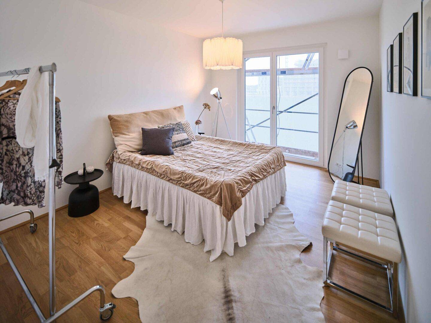 Schlafzimmer mit Doppelbett, Holzboden und großem Fenster mit Zugang zum Außenbereich.