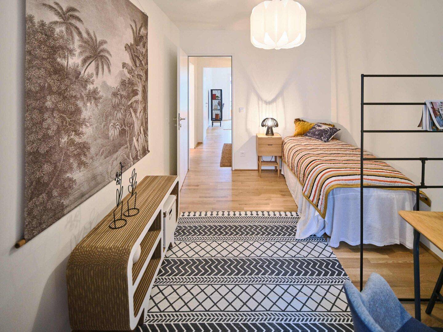Schlafzimmer mit Einzelbett, Schreibtisch und modernem Wandbild.