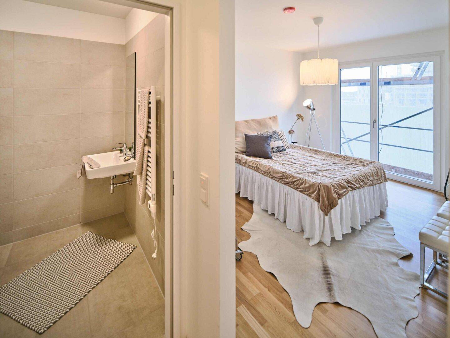 Schlafzimmer mit Holzboden und Blick auf den Eingang zu einem gefliesten Badezimmer.