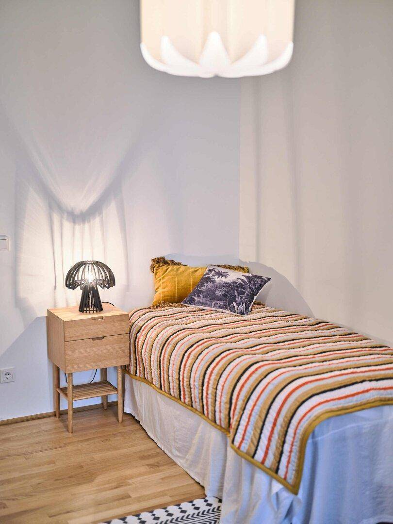 Detailansicht eines Einzelbettes mit Nachttisch und Lampe.